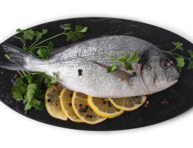 Çiğ dorado balığı, maydanoz, limon dilimleri ve beyaz üzerine izole edilmiş biberler.