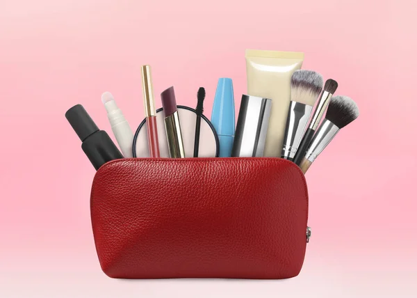 Cosmetic bag filled with makeup products on pink background