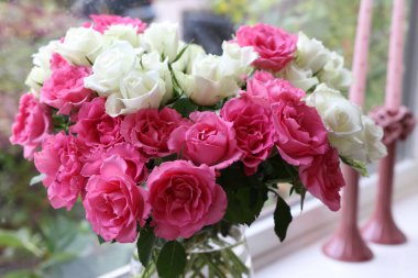 İçinde güzel bir buket gül olan vazo ve pencere pervazında mumlar, yakın plan.