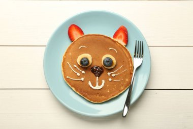 Çocuklar için yaratıcı hizmet. Krep, böğürtlen, krema, muz ve çikolatadan yapılmış tatlı bir kedi tabağı beyaz ahşap masa, üst görünüm