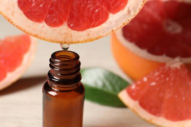Temel yağ, arka planda hafif arkaplanda greyfurttan şişeye damlıyor.