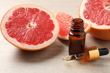 Bir şişe greyfurt yağı ve hafif ahşap masada taze meyveler.