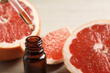 Pipetten şişeye damlayan greyfurt yağı ve arka planda taze meyveler, yakın plan