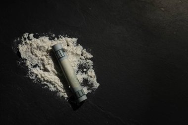 Sert uyuşturucu ve koyu dokulu arka plan üzerine yuvarlanmış dolar banknotu, üst görünüm. Metin için boşluk