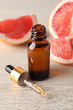 Şişede greyfurt yağı, pipet ve meyveler açık ahşap masada, yakın plan.