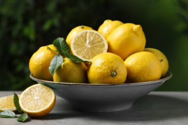 Gri masada taze limonlar ve yeşil yapraklar, yakın plan.