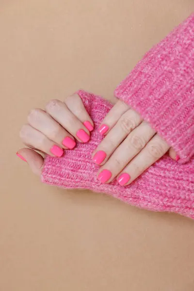 Woman showing her manicured hands with pink nail polish on dark beige background, closeup