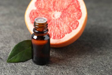 Şişede greyfurt yağı, koyu dokulu masa üzerinde yaprak ve meyve, yakın çekim