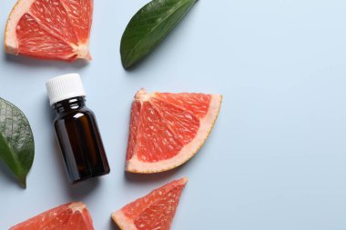 Şişede greyfurt yağı, yapraklar ve açık mavi masada meyve kesimi. Metin için boşluk