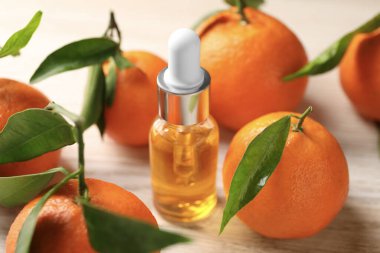 Bir şişe mandalina yağı ve beyaz ahşap masada taze meyveler, yakın plan.