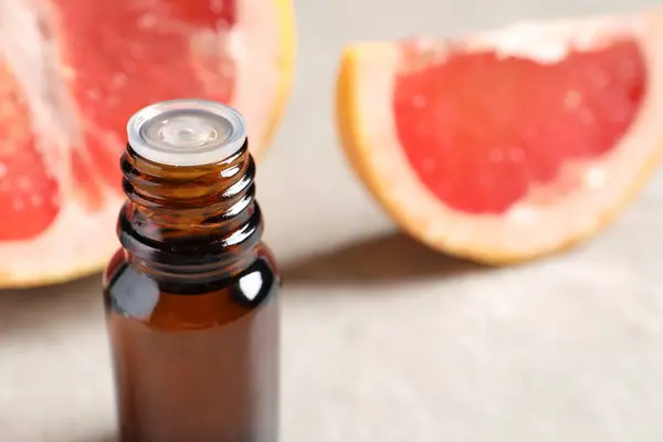 Grapefruit essential oil in bottle and fruit on light table, closeup. Space for text