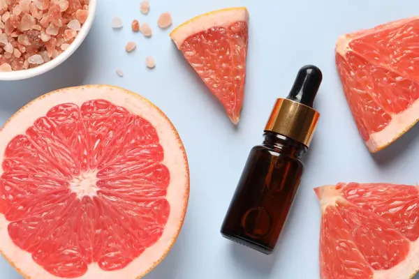 Grapefruit essential oil in bottle, sea salt and cut fruit on light blue table, flat lay