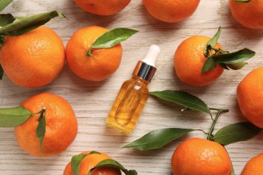 Bir şişe mandalina yağı ve beyaz ahşap masada taze meyveler.