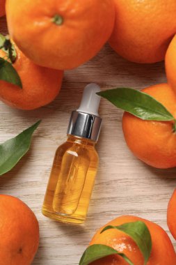 Bir şişe mandalina yağı ve beyaz ahşap masada taze meyveler.