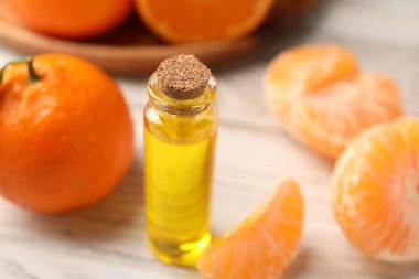 Bir şişe mandalina yağı ve beyaz ahşap masada taze meyveler, yakın plan.