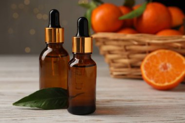 Mandalina yağı ve yeşil yaprak şişeleri beyaz ahşap masada, yakın plan.