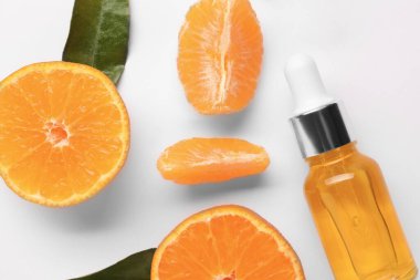 Aromatik mandalina yağı şişede, yapraklar ve narenciye meyveleri beyaz masada, düzdü.