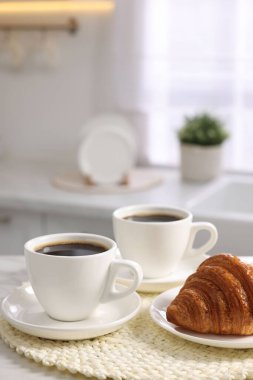 Kahvaltı mutfakta servis edilir. Bir fincan kahve ve beyaz masada taze kruvasan.