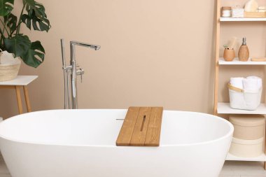 Banyodaki raflarda tahtadan yapılmış küvet ve farklı kişisel bakım ürünleri ve aksesuarlar var.