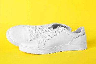 Sarı arka planda bir çift şık beyaz spor ayakkabı.