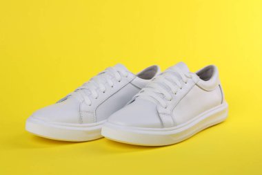 Sarı arka planda bir çift şık beyaz spor ayakkabı.