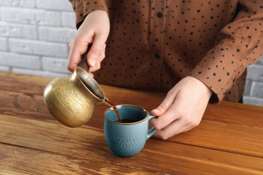 Türk kahvesi. Ahşap masada demlenmiş içeceği bardağa dolduran kadın, yakın plan.