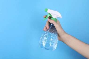 Açık mavi arka planda plastik sprey şişesi tutan kadın, yakın plan. Metin için boşluk