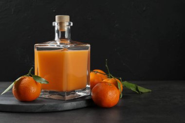 Cam şişede nefis mandalina likörü ve gri masada taze meyve, mesaj için yer var.