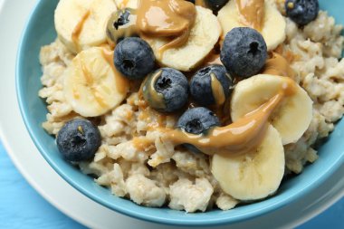 Muz, yabanmersini ve fıstık ezmeli lezzetli yulaf ezmesi açık mavi ahşap masada servis edilir.