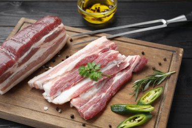 Çiğ domuz göbeği, biber, biber, biberiye ve maydanoz parçaları siyah ahşap masada, yakın plan.