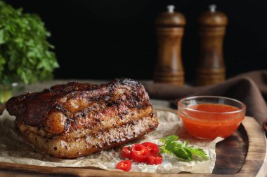 Bir parça domuz eti soslu ve ahşap masada kırmızı biberli servis ediliyor.