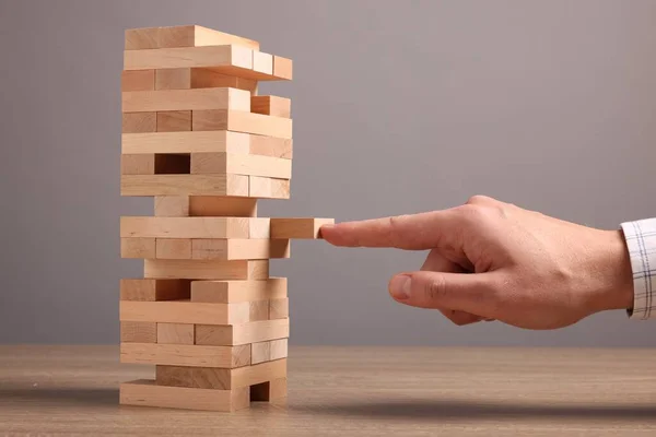 Playing Jenga. Man building tower with blocks at wooden table against grey background, closeup