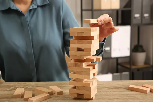 Playing Jenga. Woman building tower with blocks at wooden table indoors, closeup