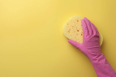 Lastik eldivenli temizlikçi sarı arka planda yeni bir sünger tutuyor. Metin için boşluk