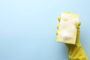 Açık mavi arka planda köpüklü kauçuk eldivenli sünger, üst manzara. Metin için boşluk