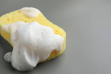 Gri arkaplanda köpüklü sarı sünger, yakın plan.