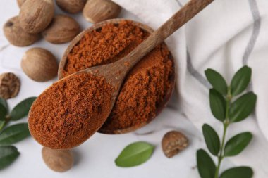 Nutmeg tozu, tohumlar ve yeşil dallar beyaz masada, düz yerde.