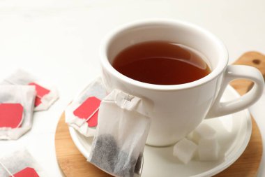 Çay poşetleri ve bir fincan sıcak içecek beyaz masada, yakın plan.