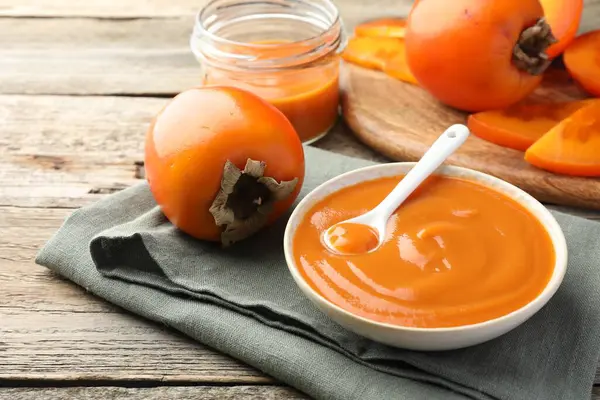 Lezzetli hurma reçeli ve ahşap masada taze meyve.