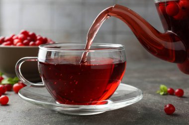 Sıcak yaban mersini çayını cam fincana ve taze böğürtlenleri açık gri desenli masaya döküyorum. Yakın plan.