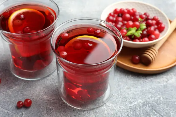 Lezzetli sıcak kızılcık çayı, bardakta limon ve açık gri dokulu masada taze böğürtlen.