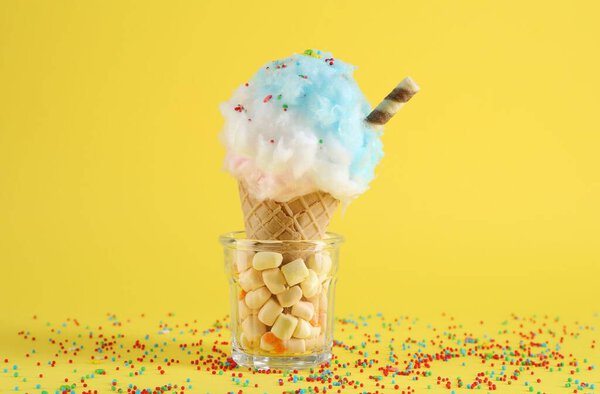 Sweet cotton candy in waffle cone on yellow background, closeup