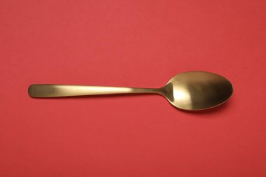 Kırmızı arka planda parlak bir altın kaşık.