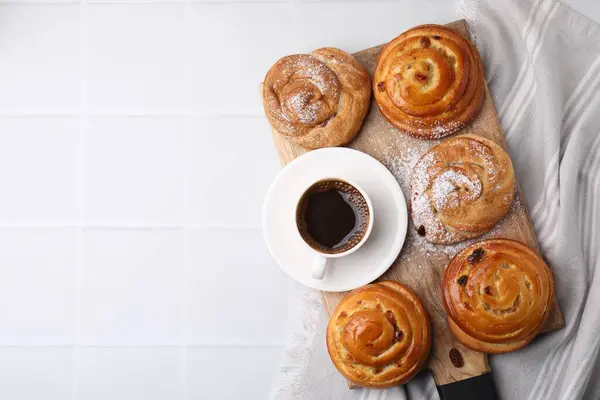 Sweet buns. Delicious rolls with raisins, powdered sugar and coffee cup on white tiled table, top view. Space for text
