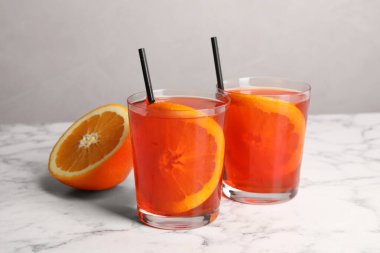 Aperol spritz kokteyli, portakal dilimleri ve beyaz mermer masa üzerinde pipetler.