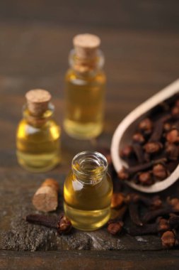 Şişelerdeki karanfil yağı ve ahşap masada kurumuş tomurcuklar, yakın plan.