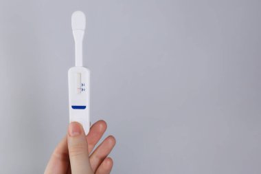 Açık gri arka planda tek kullanımlık ekspres test yapan kadın, yakın plan. Metin için boşluk