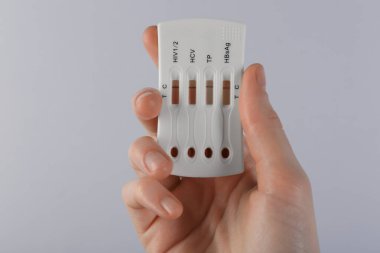 Açık gri arka plan üzerinde tek kullanımlık çoklu enfeksiyon ekspres testi yapan kadın, yakın plan.