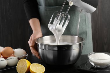 Siyah masada el çırpıcı ile krem şanti yapan kadın, yakın plan.