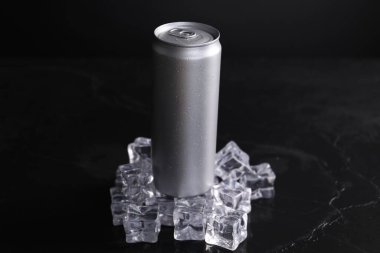 Alüminyum kutu enerji içeceği ve buz küpleri siyah masada.